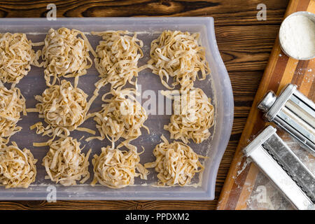 Faire des pâtes fettuccine frais avec une vue de dessus d'une table de cuisine avec des portions de pâtes séchant sur un plateau à côté d'un coupe-pâtes et f Banque D'Images