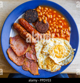 Vue de dessus d'un petit-déjeuner anglais complet de bacon frit oeufs haricots et saucisses sur une table de café. Banque D'Images