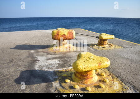 Grèce, la charmante et belle île de Sikinos. Trois bornes jaunes pour l'amarrage des ferries, sur le bord de la jetée en béton au port des îles. Banque D'Images