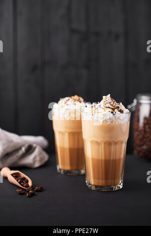 Café Latte au caramel glacé dans un grand verre avec du sirop de chocolat et crème fouettée. Fond en bois foncé avec copie espace. Banque D'Images
