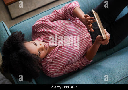 Vue de dessus de Woman Lying On Sofa At Home Watching Movie On Digital Tablet Banque D'Images