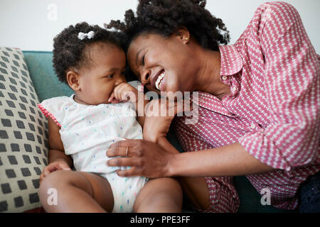 Mère couchée sur un canapé à la maison jouer avec bébé fille Banque D'Images