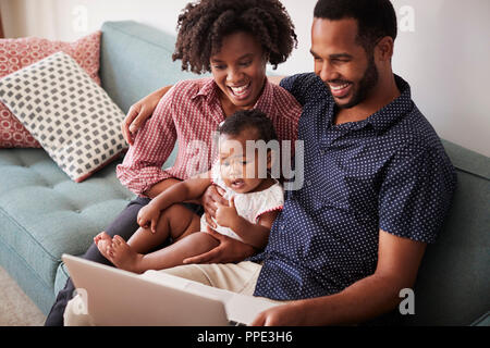 Famille avec Baby Daughter Sitting on Sofa At Home Looking At laptop computer Banque D'Images