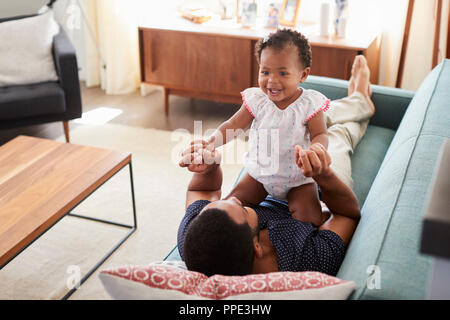 Père couché sur un canapé à la maison jouer avec bébé fille Banque D'Images