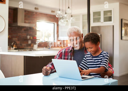 Grand-père et petit-fils assis autour de la table à la maison Using Laptop Together Banque D'Images