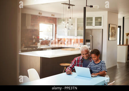 Grand-père et petit-fils assis autour de la table à la maison Using Laptop Together Banque D'Images