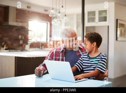 Grand-père et petit-fils assis autour de la table à la maison Using Laptop Together Banque D'Images