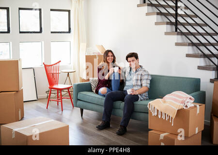 Portrait Of Happy Couple reposant sur canapé entouré par des boîtes à New Home le jour du déménagement Banque D'Images