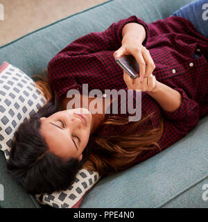 Vue de dessus de Woman Lying On Sofa At Home Using Mobile Phone Banque D'Images