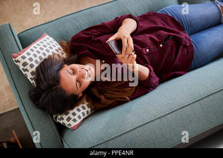 Vue de dessus de Woman Lying On Sofa At Home Using Mobile Phone Banque D'Images