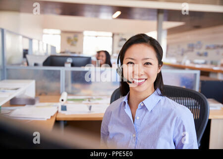 Young Asian woman travaillant dans un centre d'appel souriant pour appareil photo Banque D'Images