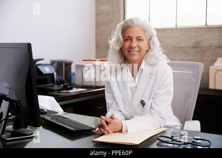Senior female doctor sitting at desk in office, portrait Banque D'Images