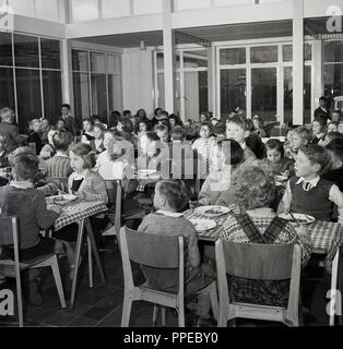 Années 1950, historiques, l'école primaire des enfants assis ensemble à des tables en bois ayant leur école le dîner (déjeuner) England, UK. Banque D'Images