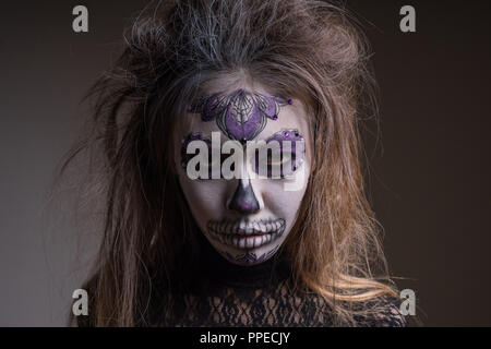 Portrait d'une fille avec un masque peint d'une personne morte sur son visage, isolé sur un fond sombre. Halloween de Banque D'Images