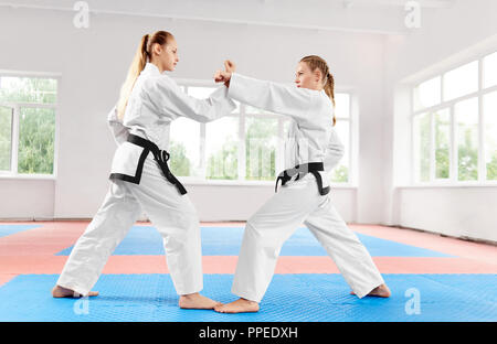 Deux jeunes filles athlétiques à l'aide de techniques de karaté en difficulté dans des classes de karaté. Strong Women wearing en kimono blanc et les ceintures noires faisant concours parmi eux-mêmes. Concept de sport. Banque D'Images