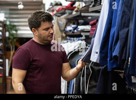 Man looking at shirts, vestes et chaussures d'essayer dans un magasin de mode Banque D'Images