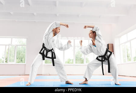Deux femme sportive karaté combats sur la formation en école d'arts martiaux. Strong Women wearing en kimono blanc et les ceintures noires faisant concours parmi eux-mêmes. Style de vie sain et de sport concept. Banque D'Images