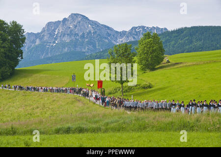 Corpus Christi procession à travers les plaines et les champs de la colère d'Hoeglwoerth avec le Hochstaufen en arrière-plan, la Bavière, l'Allemagne, le Saint Sacrement est porté par le prêtre, qui passe sous le 'ciel'. Banque D'Images