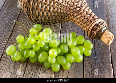 Raisin blanc à l'ancienne bouteille verre enveloppé en osier sur table en bois Banque D'Images