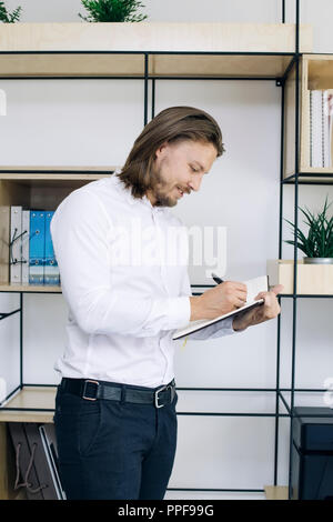 Young businessman taking notes sur son ordre du jour tout en standing in office Banque D'Images