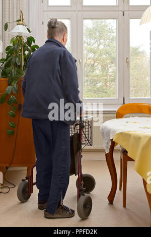 Vieille Femme qui se déplace dans son salon avec 3 roues walker. Une aide à la mobilité pour les personnes ayant des problèmes d'équilibre et de force dans les petits espaces. Banque D'Images