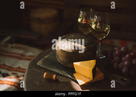 Tranches de fromage avec du vin et du raisin sur planche à découper en bois Banque D'Images