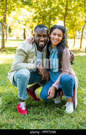 African American couple hugging, accroupis et looking at camera in park Banque D'Images