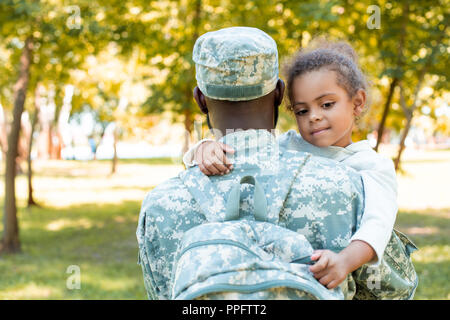 Soldat afro-américain en uniforme militaire holding daughter in park Banque D'Images