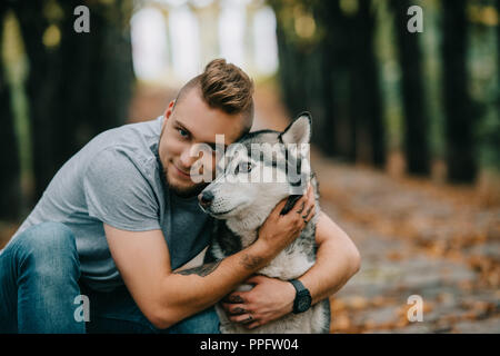 Young smiling man hugging dog husky in park Banque D'Images