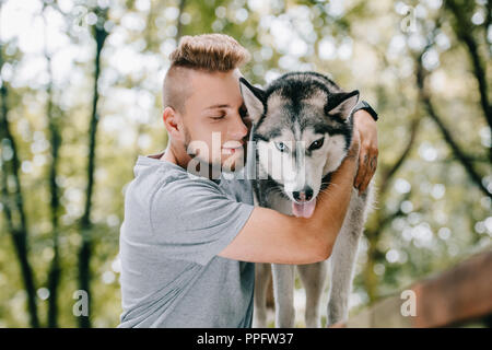 Young man hugging dog husky in park Banque D'Images