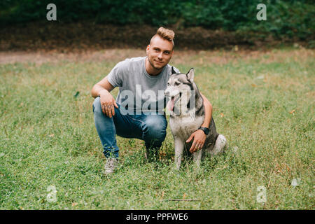 Jeune homme serrant avec chien husky de Sibérie dans park Banque D'Images