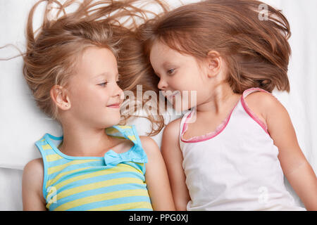 Deux petites soeurs dorment ensemble, avec des expressions positives à l'autre, vêtu de vêtements décontractés, ont de bonnes relations. Meilleure femelle pour enfants fr Banque D'Images