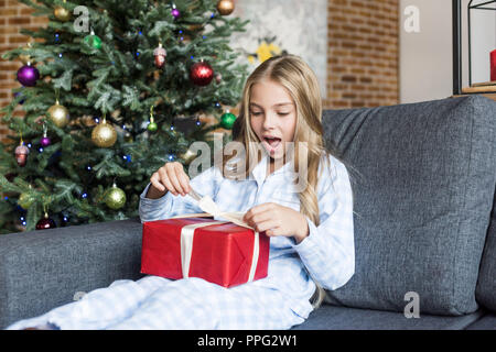 Surpris en pyjama enfant cadeau de Noël d'ouverture tout en restant assis sur la table Banque D'Images