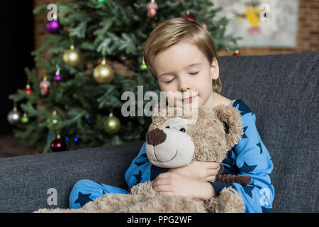 Mignon petit enfant en pyjama hugging teddy bear pendant le sommeil et assis dans le canapé Banque D'Images