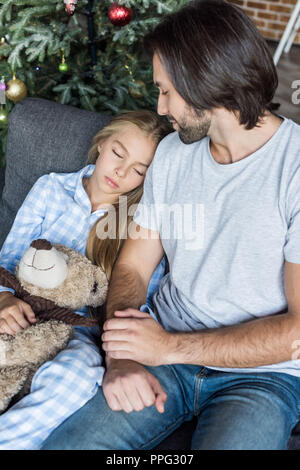 Portrait de père et fille cute dans pajamas holding teddy bear et dormir sur la table à l'époque de Noël Banque D'Images