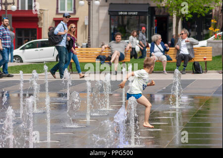 Garçon s'amusant dans un jeux d'eau Fontaine, qui court entre les jets d'eau et l'attention des spectateurs de dessin. Les jardins de l'Hôtel de ville, la ville de Québec. Banque D'Images