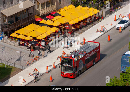 Un double-decker hop-on hop-off bus sur une visite guidée en ville basse (Basse-Ville). Parasols jaunes sur une terrasse de café. La ville de Québec, Québec, Canada Banque D'Images