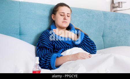 Portrait de jeune femme malade en peignoir au lit et tenant la main sur la poitrine et la gorge douloureuse Banque D'Images