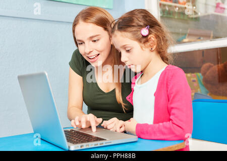La femme comme une aide à l'apprentissage de l'enseignant tout en fille à ordinateur portable. Ordinateur en maternelle Banque D'Images