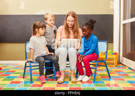 La femme comme une aide familiale et les enfants s'amuser avec l'ordinateur tablette comme un ebook en maternelle Banque D'Images