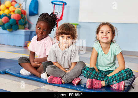 Trois jeunes filles en amis sont assis dans la salle de sport de l'école maternelle multiculturelle Banque D'Images