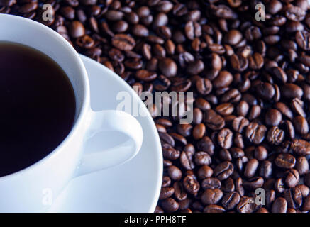 Vue de dessus de tasse de café noir dans une tasse blanche assise sur un lit de grains de café Banque D'Images