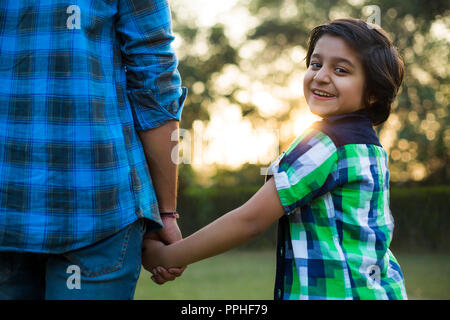 Vue arrière d'un happy boy holding hand de son père debout dans parc. Banque D'Images