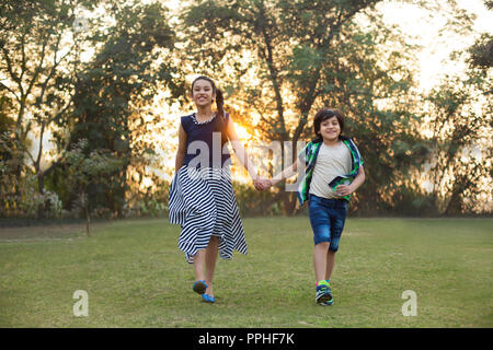 Happy brother and sister walking in park se tenant la main avec la lumière du soleil dans l'arrière-plan. Banque D'Images