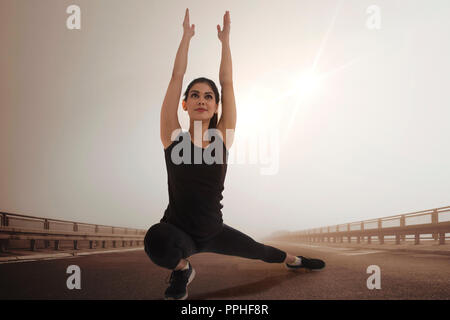 Jeune femme en tenue de sport faire des exercices d'étirement en plein air avec le soleil en arrière-plan. Banque D'Images