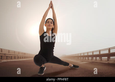 Jeune femme en tenue de sport faisant du yoga en plein air avec le soleil en arrière-plan. Banque D'Images