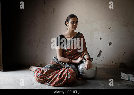 Beau village femme assise sur le sol avec un pot d'acier dans une ancienne chambre à l'hôtel. Banque D'Images