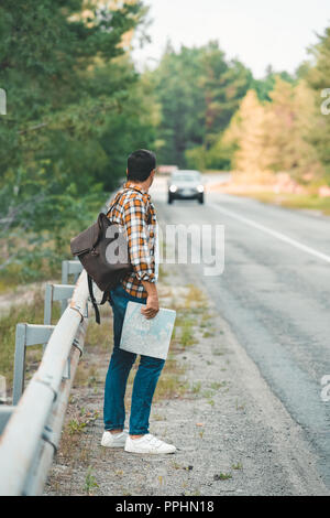 Vue de côté de l'homme avec sac à dos et une carte debout sur route en voyageant seuls Banque D'Images