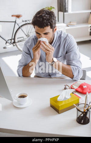 Sick woman blowing nose in tissue in office Banque D'Images