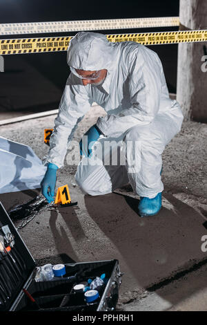 Criminologue mâle en tenue de protection et des gants en latex de la collecte des preuves au lieu de crime avec corpse Banque D'Images